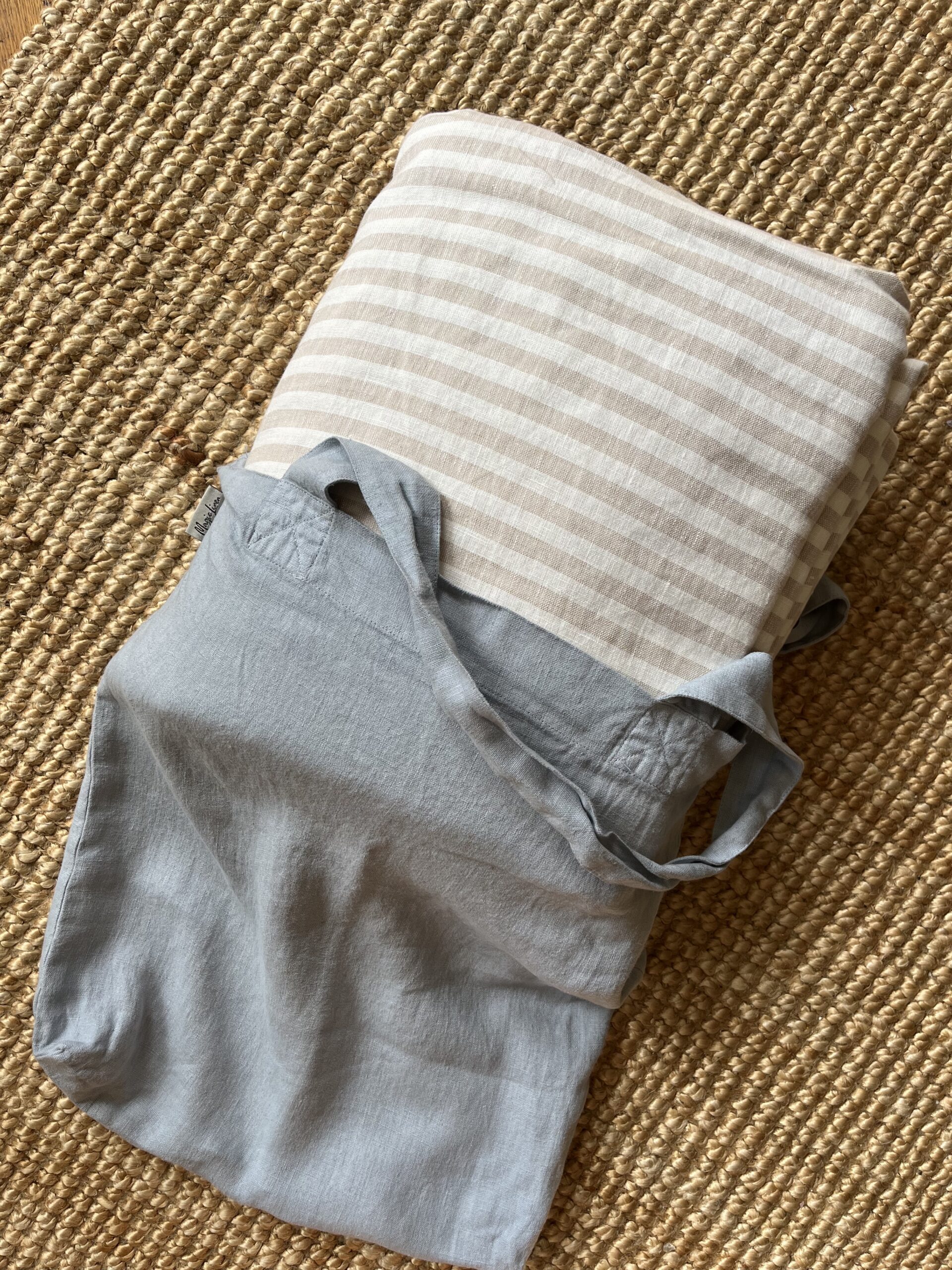 Folded beige and white striped fabric with a blue cloth bag on a woven mat background.