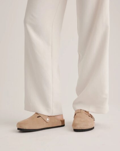 Person wearing white pants and beige slip-on clogs with a single button detail on the side.
