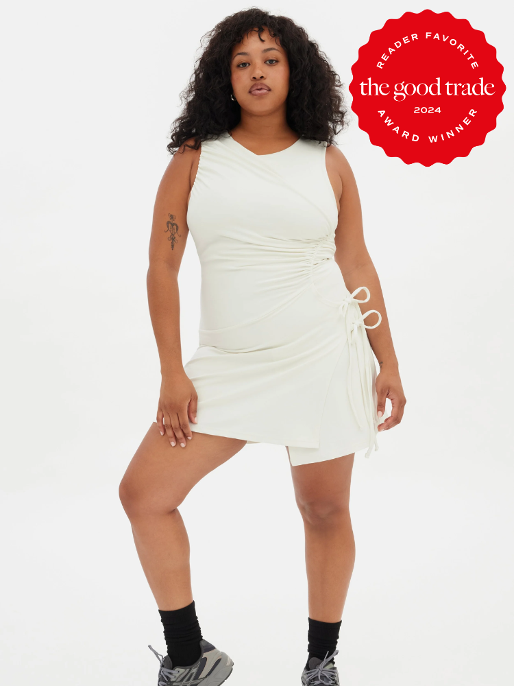 A model wearing a white ruched athleisure dress from Girlfriend Collective. 
