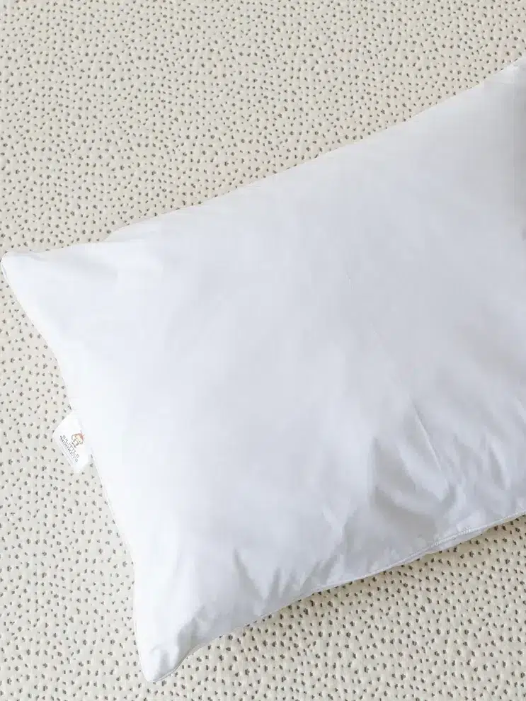 A plain white pillow is placed on a dotted beige surface.