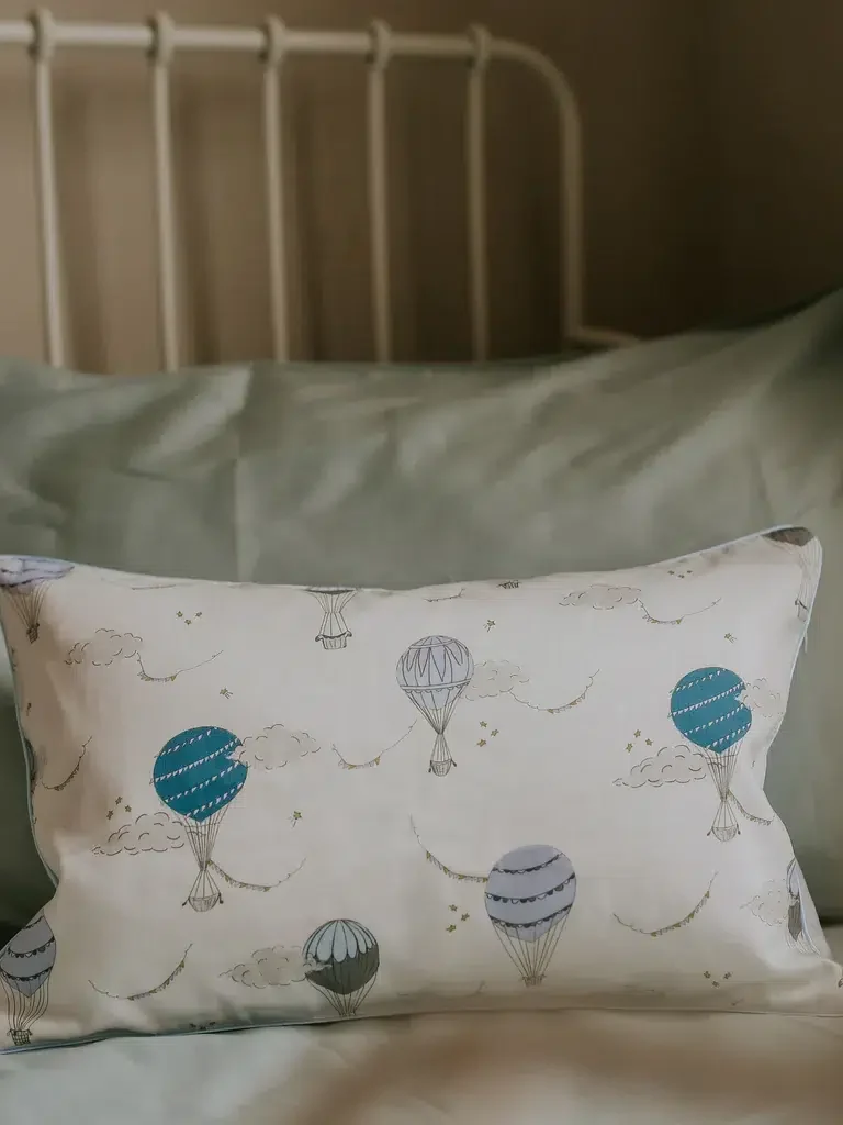 A decorative pillow with hot air balloon designs on a bed with green bedding and a white headboard.