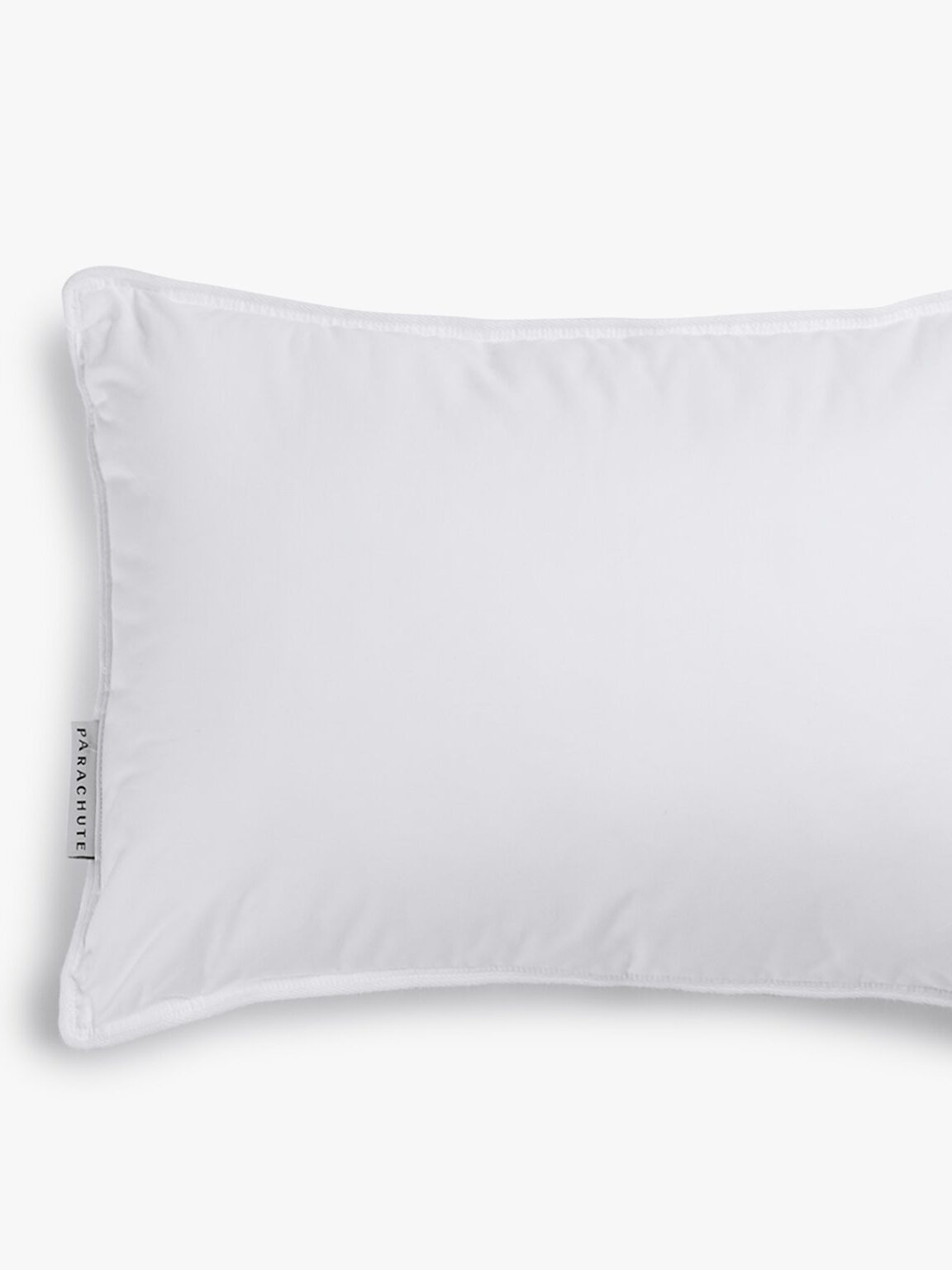A rectangular white pillow with a brand tag on the left side, placed against a white background.