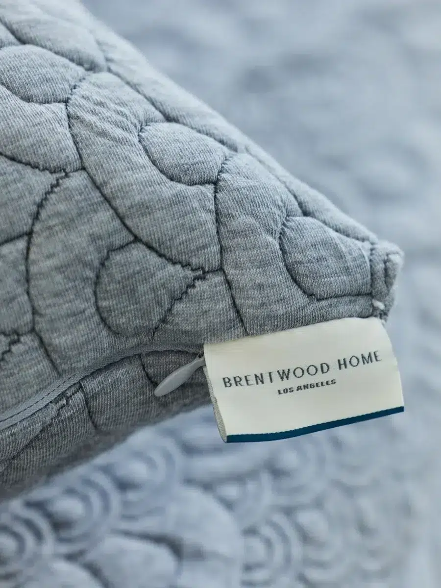 Close-up of a gray pillow with intricate patterns and a visible tag that reads "Brentwood Home Los Angeles.