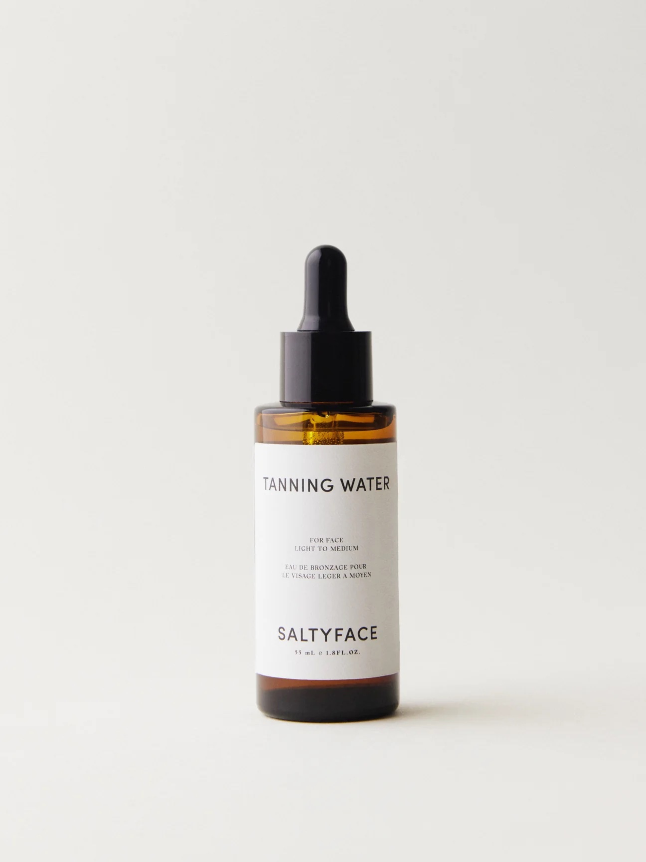 A bottle of Saltyface Tanning Water with a black dropper lid and a white label, designed for use on the face.