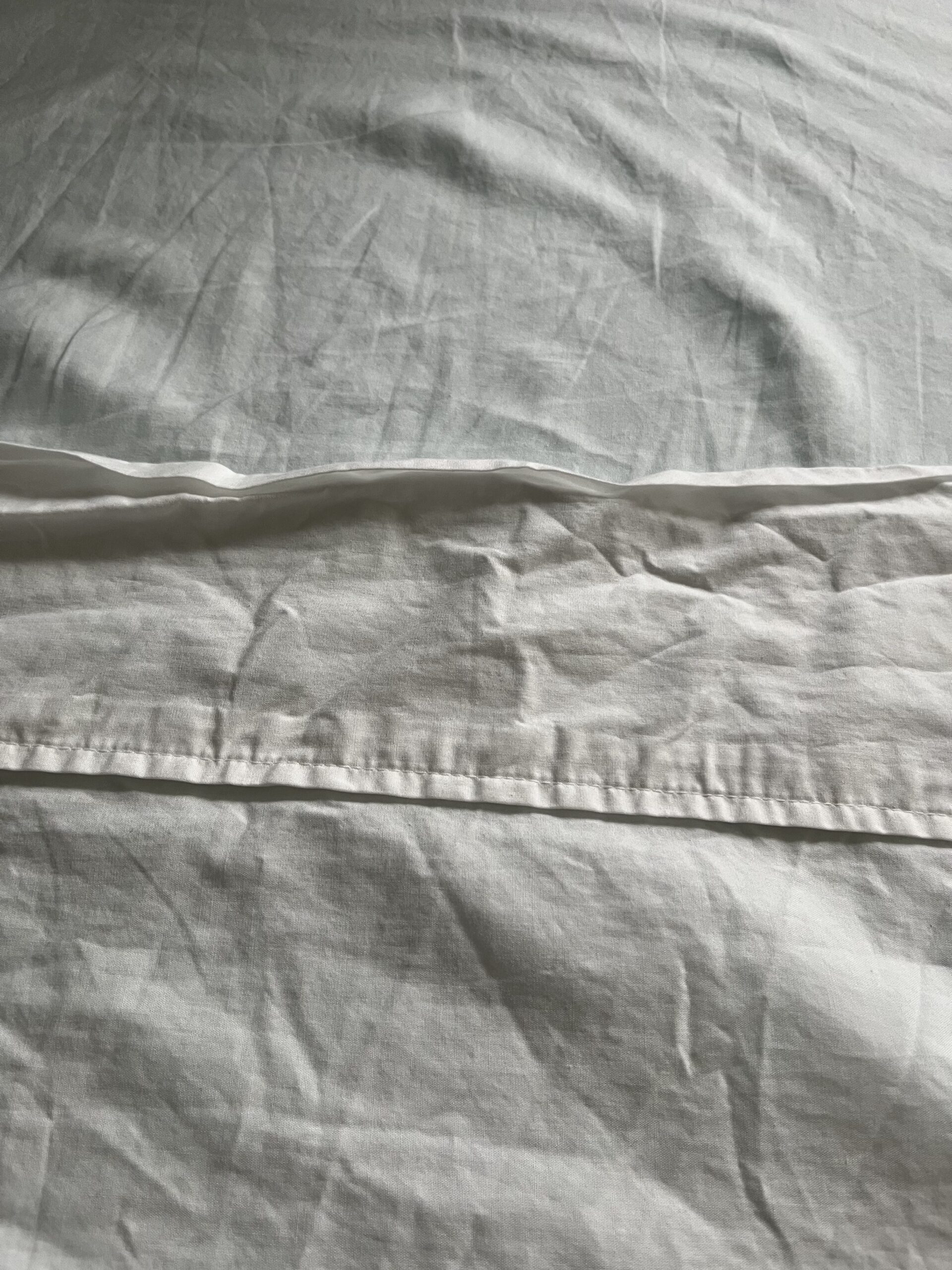 Close-up of a white, somewhat wrinkled bed sheet with a horizontal seam near the upper third of the image.