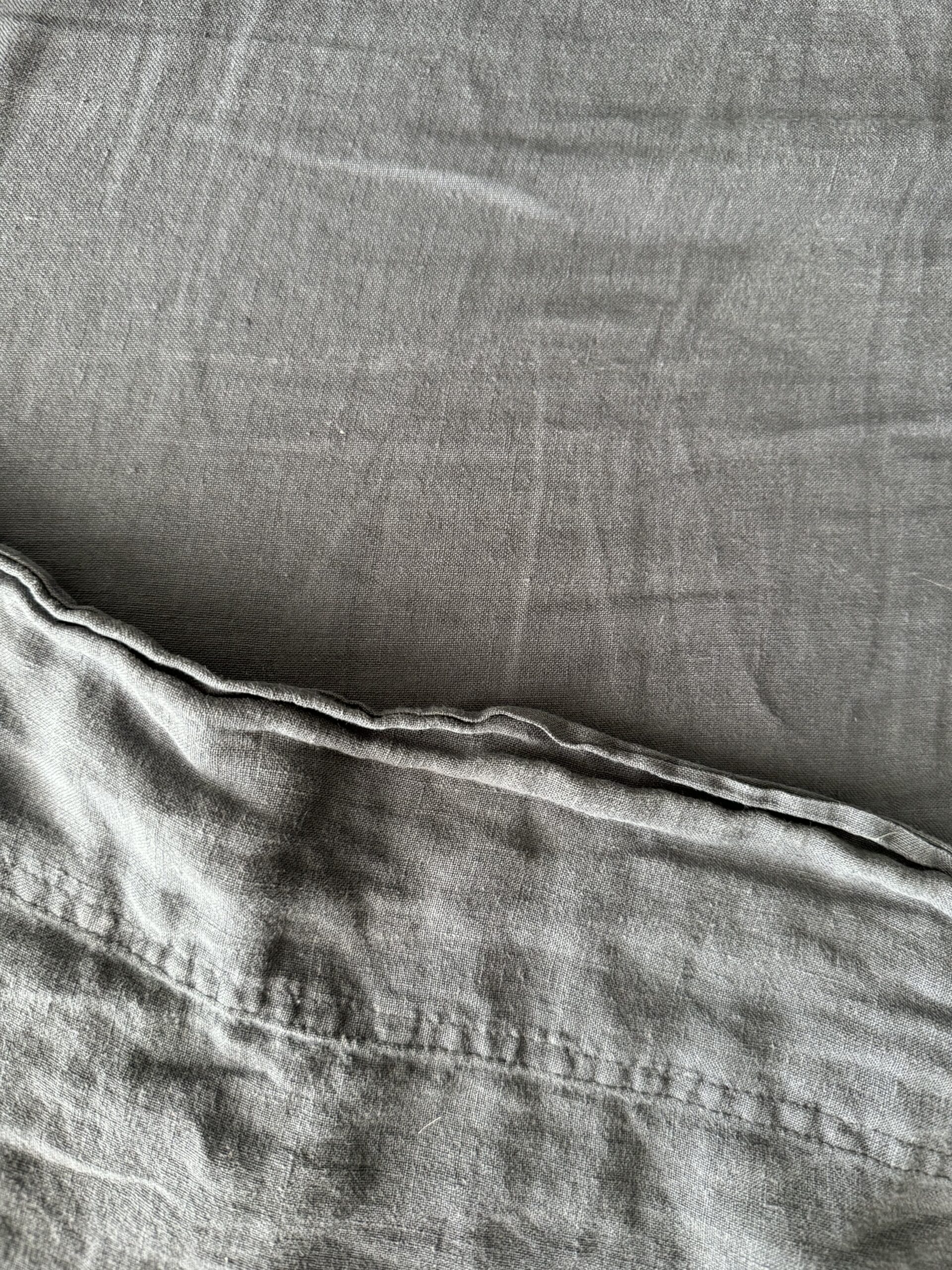 Close-up of a gray fabric with visible stitching, slight wrinkles, and a seam running horizontally near the bottom of the image.