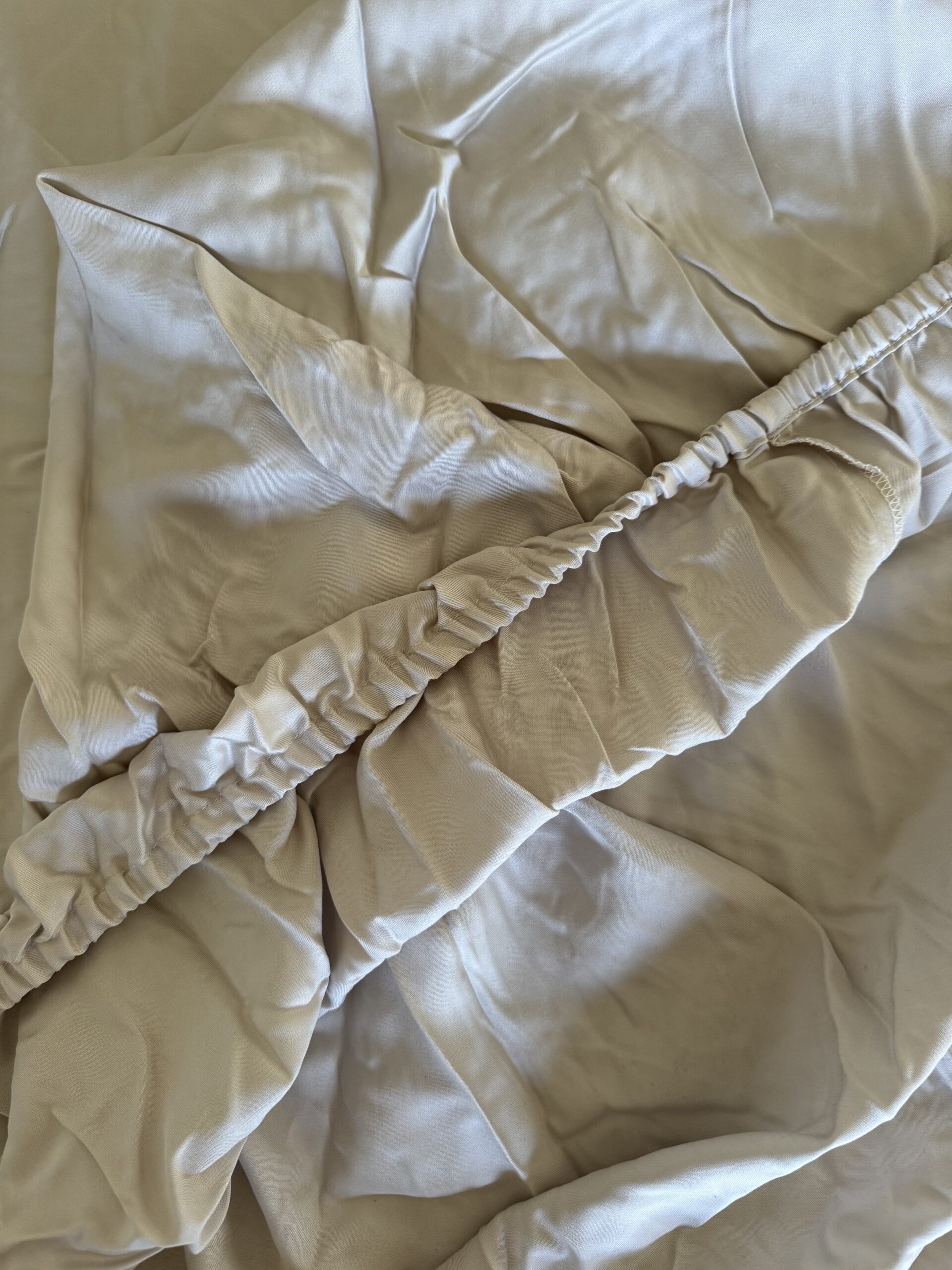 A beige fitted sheet crumpled and folded on itself, showing elastic edges and creases along the fabric.