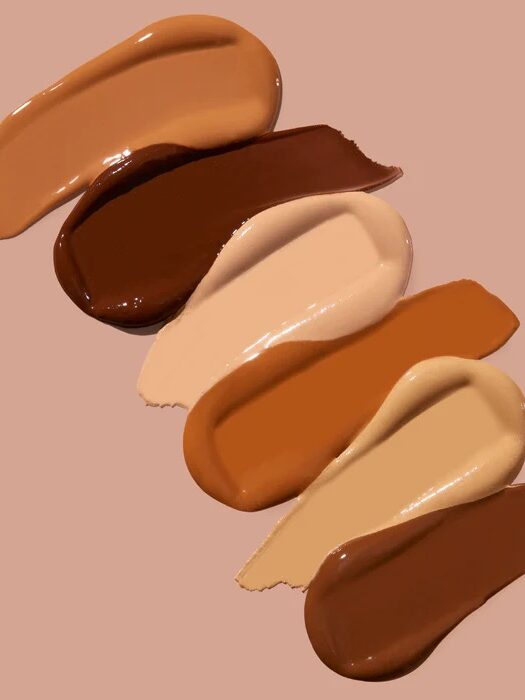 Various shades of foundation makeup swiped against a beige background, showcasing a range of light to dark tones.