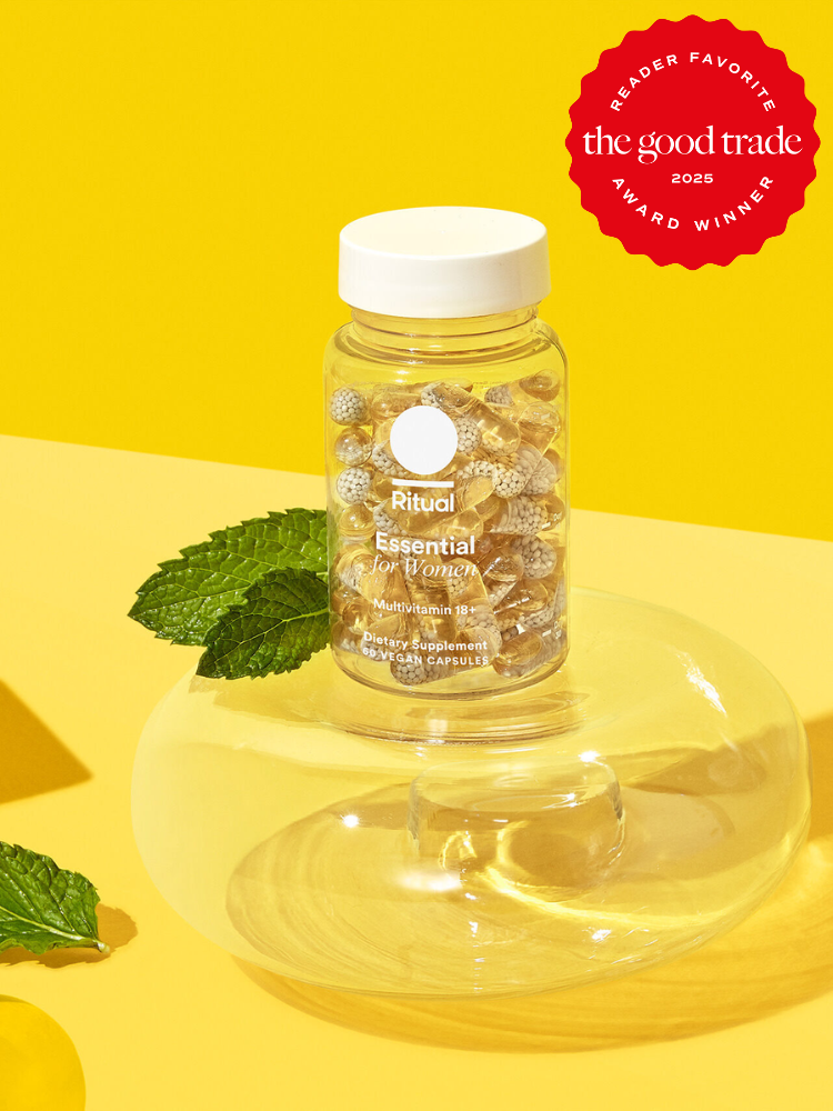 A bottle of Ritual Essential multivitamins for women on a glass stand with mint leaves nearby, set against a yellow background. A "Reader Favorite" award badge from "The Good Trade" is in the corner.