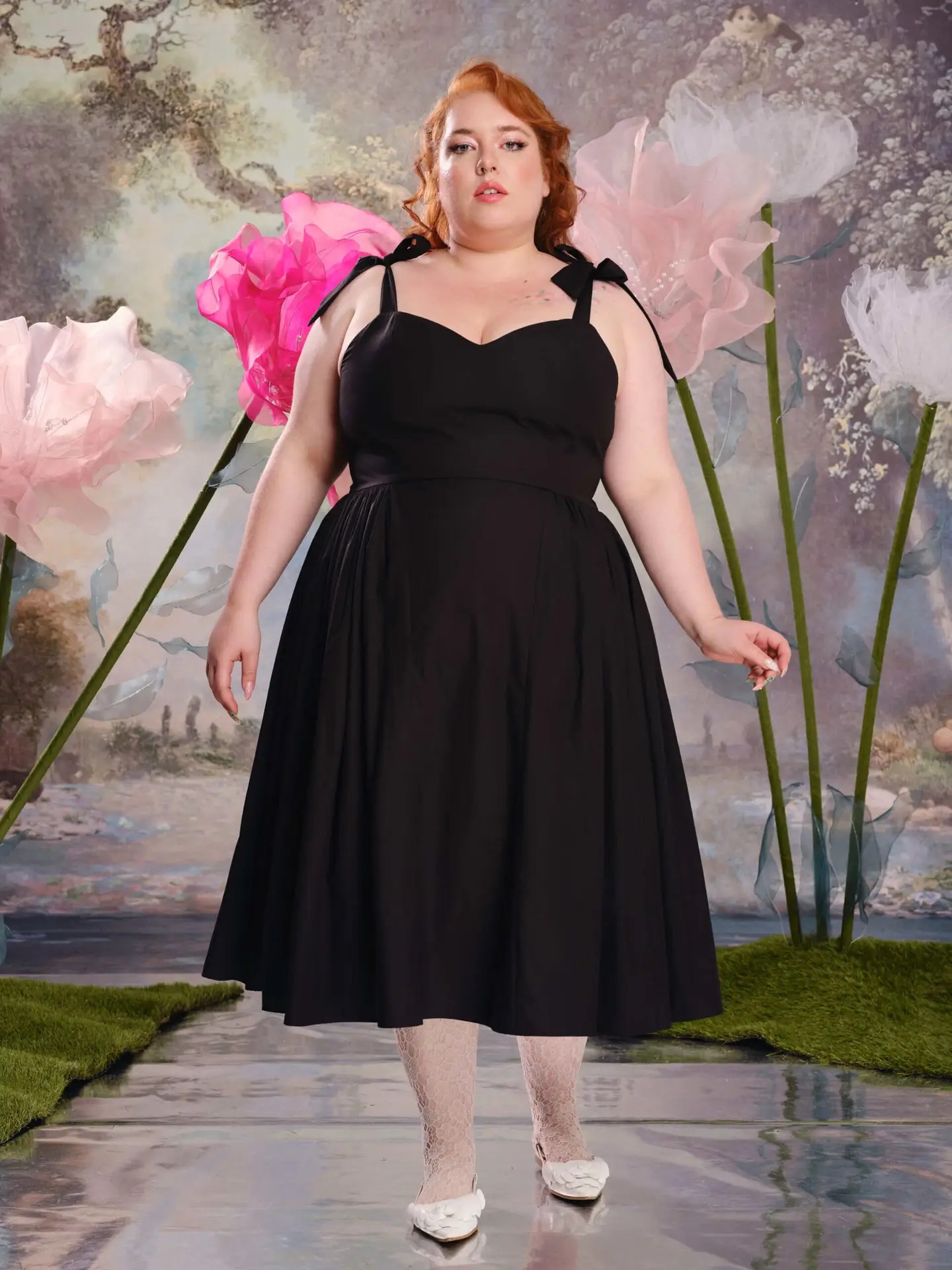 A plus size model wearing a black sweetheart a-line dress with tie straps from Loud Bodies.