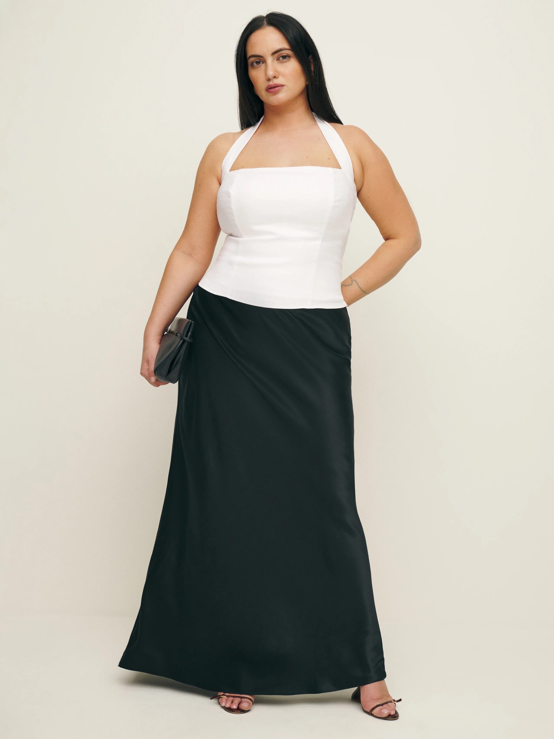 A plus size model wearing a white halter top and a black silk skirt from Reformation.