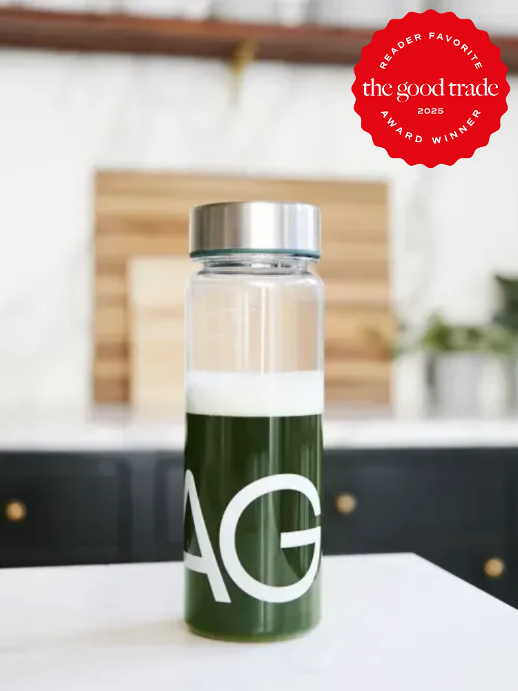 A clear bottle with a silver cap filled with dark green liquid, labeled "AG," stands on a white surface. A red badge in the image corner reads, "the good trade 2023 award winner.