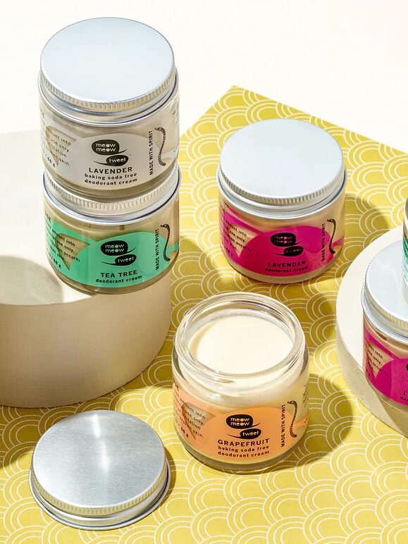A display of nine jar candles in various scents, including lavender, tea tree, and grapefruit, arranged on yellow patterned and white surfaces.