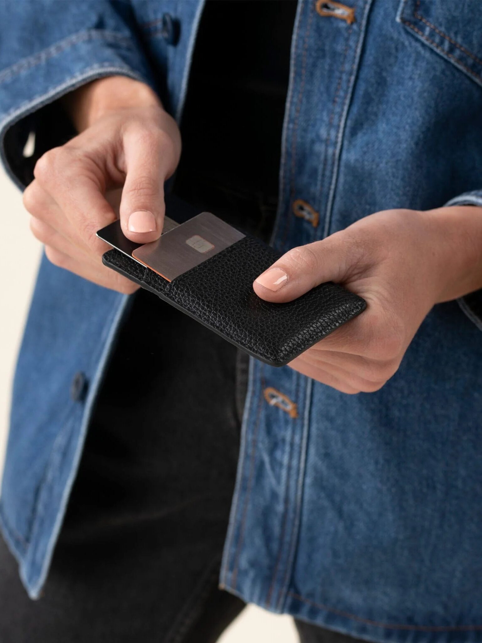 A close up of a model pulling out a card from a Nisolo card holder.