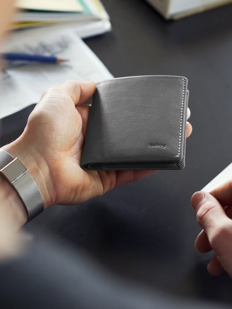 A hand holding a Bellroy wallet.