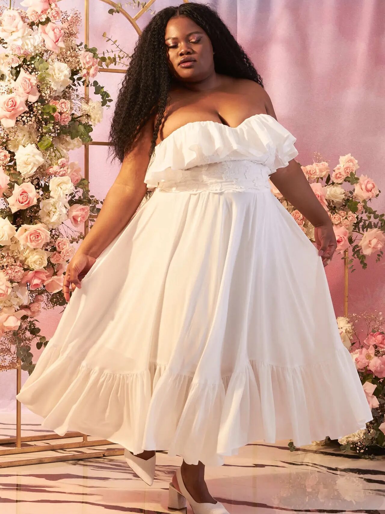 A plus size model wearing a white strapless ruffled dress from Loud Bodies.