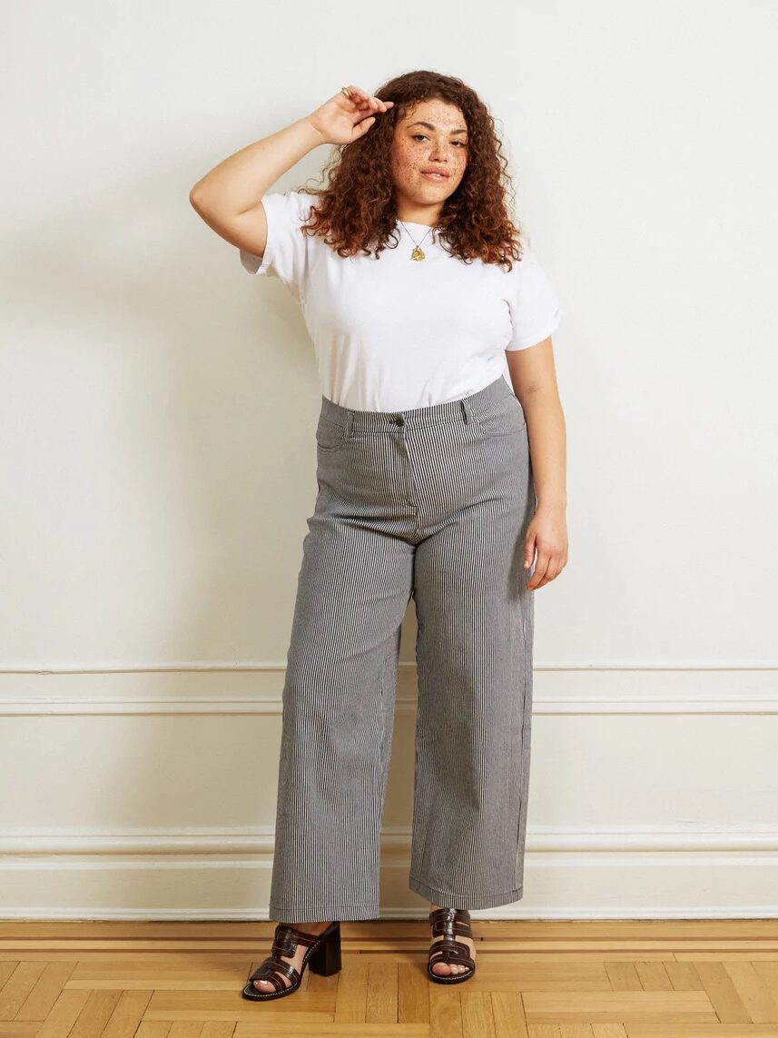 A plus size model wearing a white t-shirt and grey pinstripe pants from Loup.