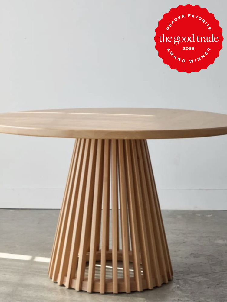 Round wooden table with a slatted, conical base on a concrete floor. A red badge in the top right corner reads "Reader Favorite, The Good Trade, 2025 Award Winner.