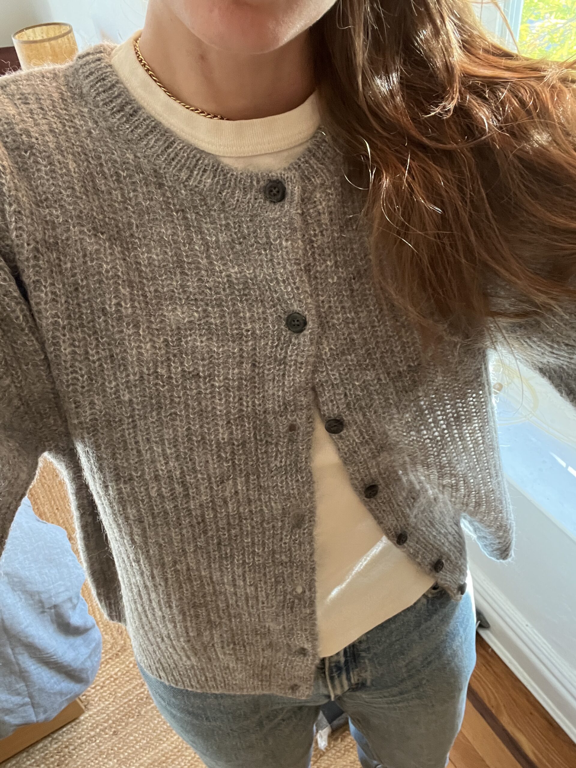 A selfie closeup of a gray cardigan with black buttons on a woman whose light brown hair is visible on one shoulder. 