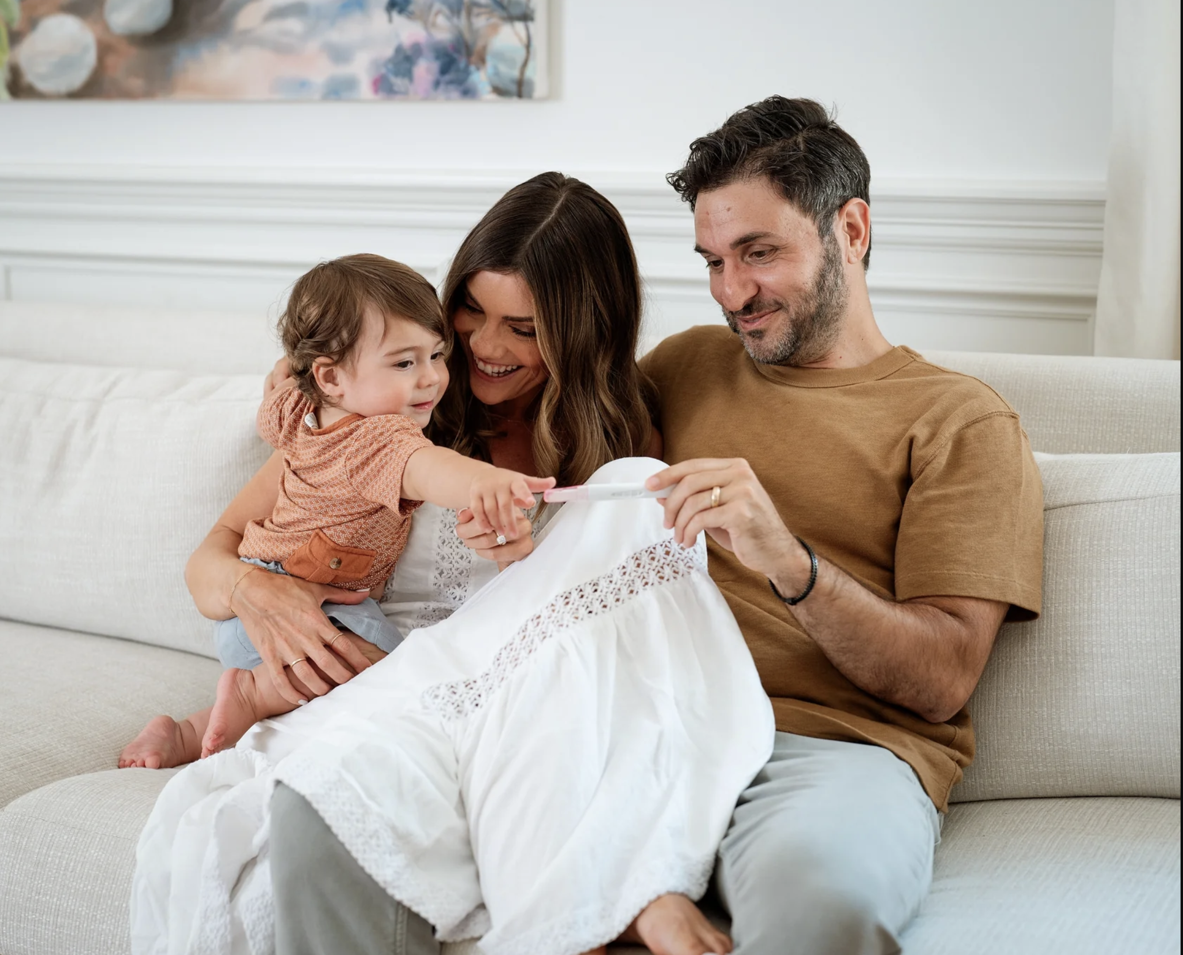 A family seated together, smiling at a pregnancy test. 