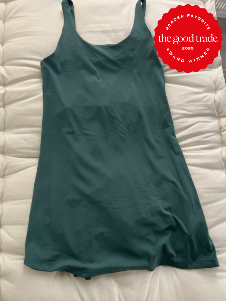 A dark green camisole dress laid flat on a white cushion, with a red award badge in the top right corner.