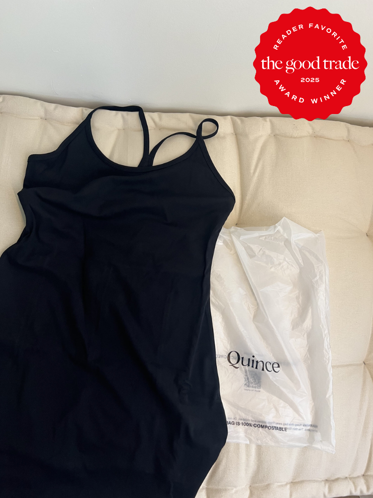 Black tank top on a cream cushion next to a white plastic bag with "Quince" branding, featuring a red award badge in the top right corner.