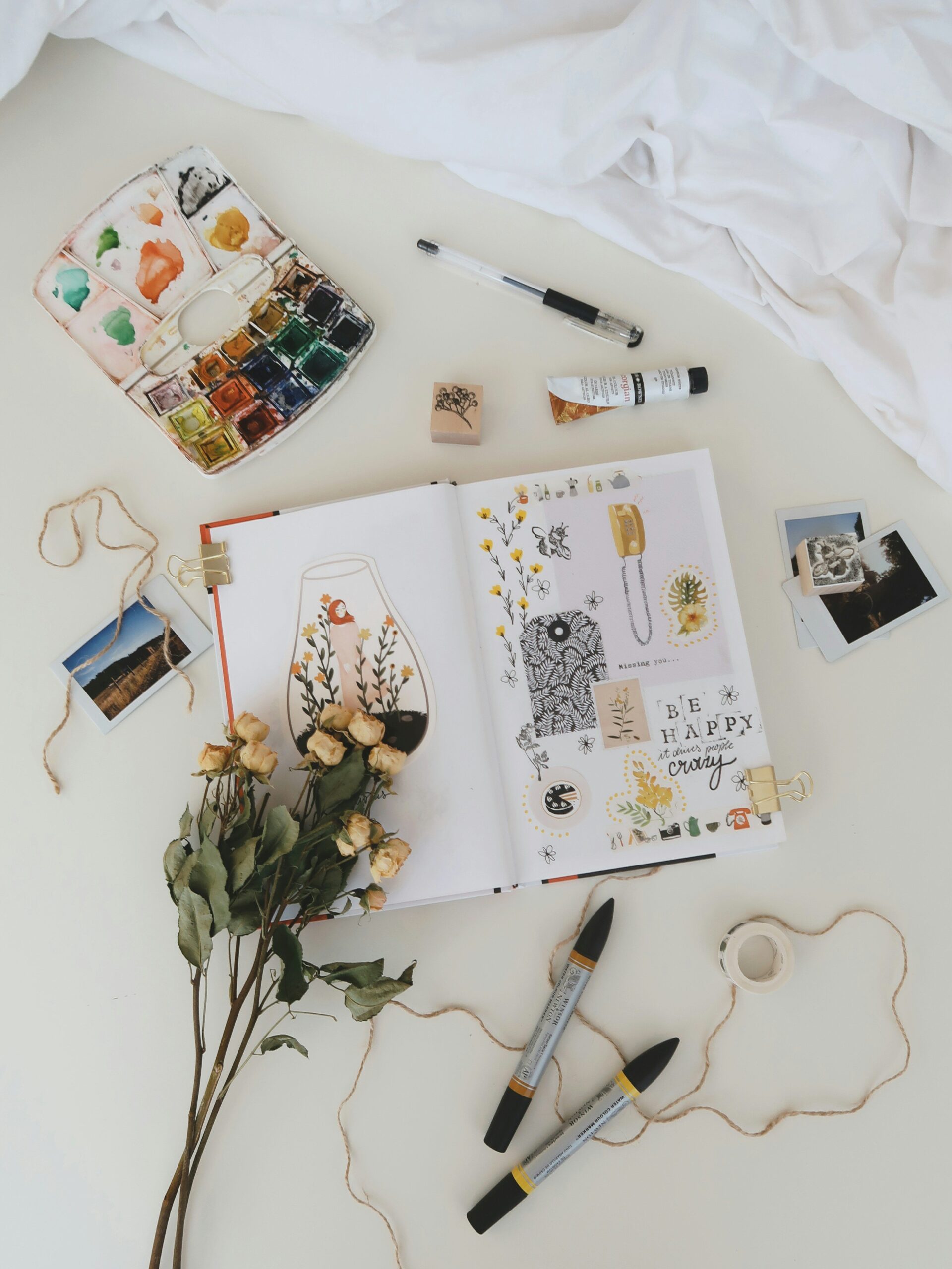 A variety of arts and crafts materials surrounding an open scrapbooking journal.