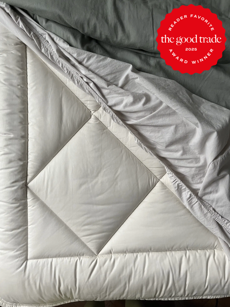 A neatly arranged white comforter with a folded corner showing a quilted pattern. A red award badge in the top right corner reads "Reader Favorite the good trade 2025 Award Winner.