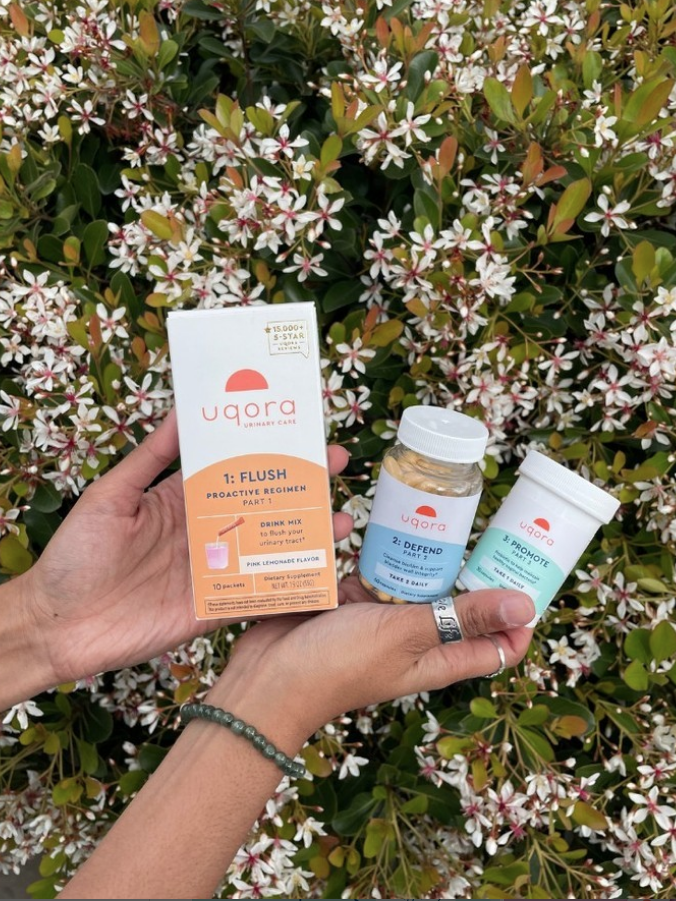 Hands holding Uqora products against a background of flowering shrubs.