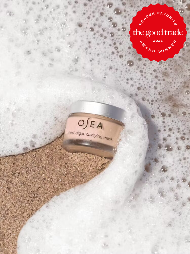 OSEA red algae clarifying mask jar on sandy beach, surrounded by sea foam, with a red "The Good Trade Reader Favorite 2025 Award Winner" seal.