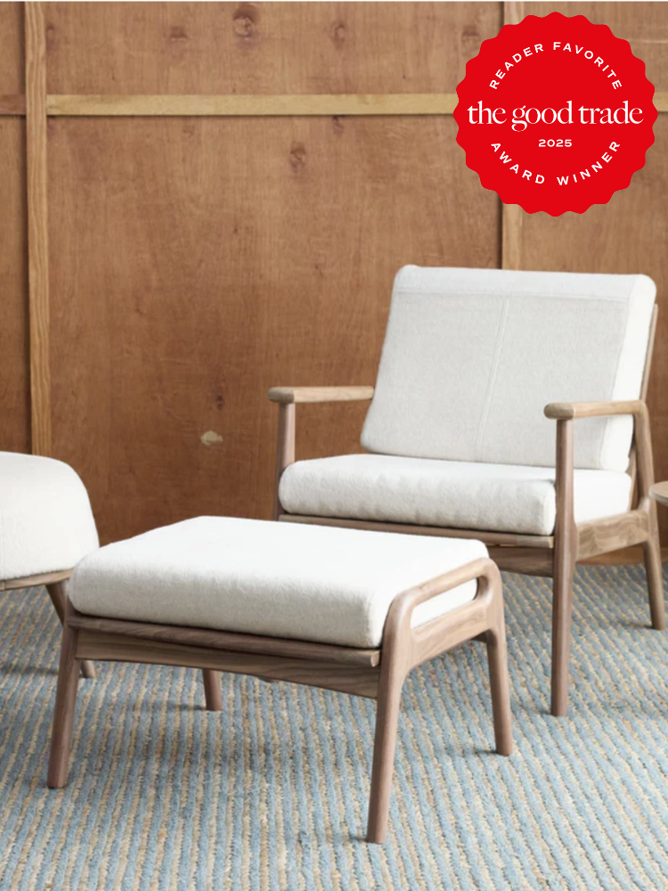 Wooden armchair with white cushions and matching ottoman on a blue-striped rug. A "Reader Favorite The Good Trade Award Winner 2025" badge is in the top right corner.