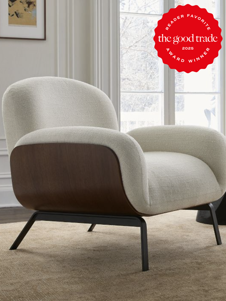 A modern armchair with plush, light-colored upholstery and dark wooden accents is placed on a carpeted floor in a bright room. A red award badge is present in the upper right corner.