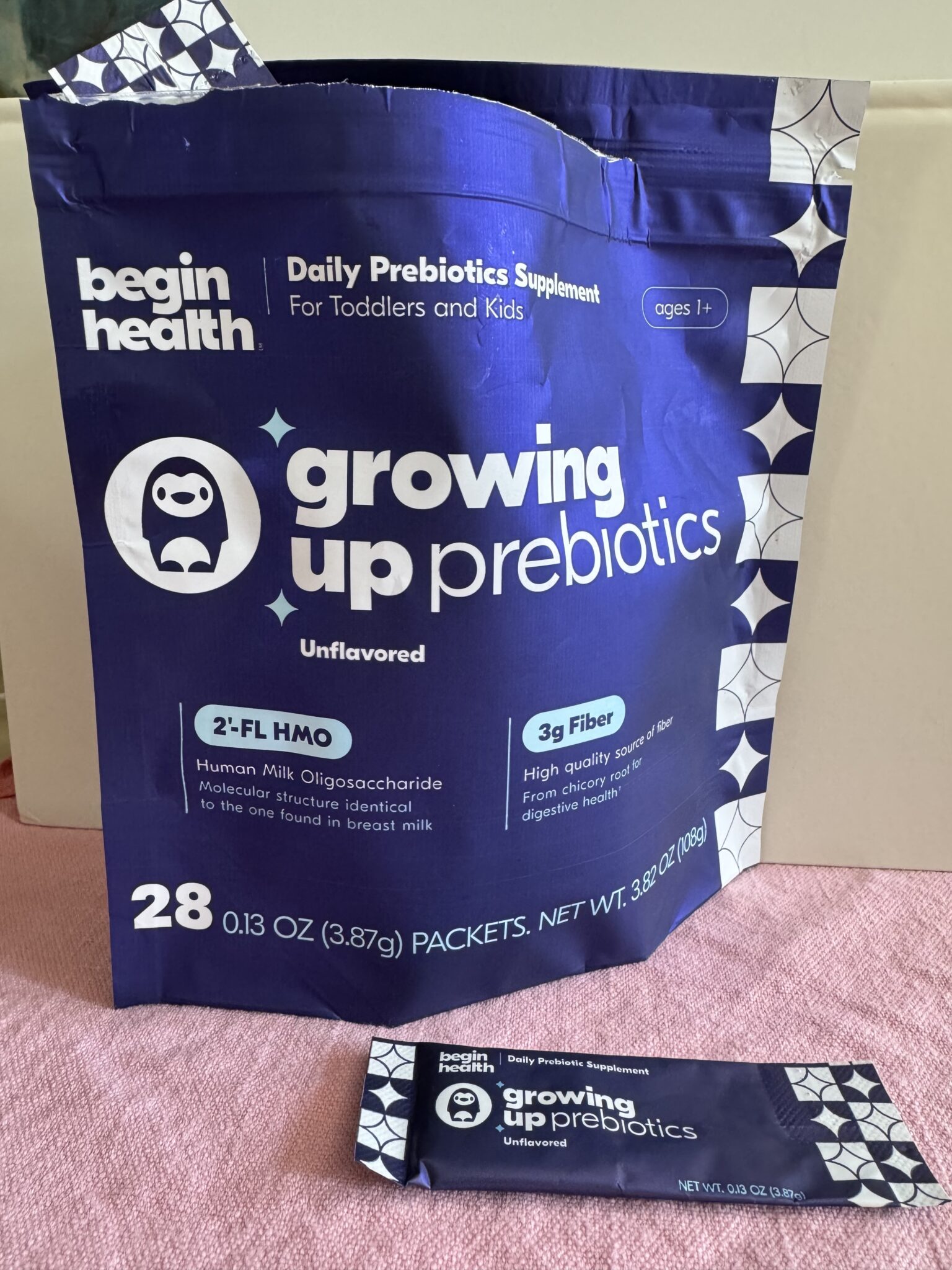 A package of "growing up prebiotics" daily supplement for toddlers and kids, showing 28 unflavored packets with 3g fiber and 2'-FL HMO, by begin health.