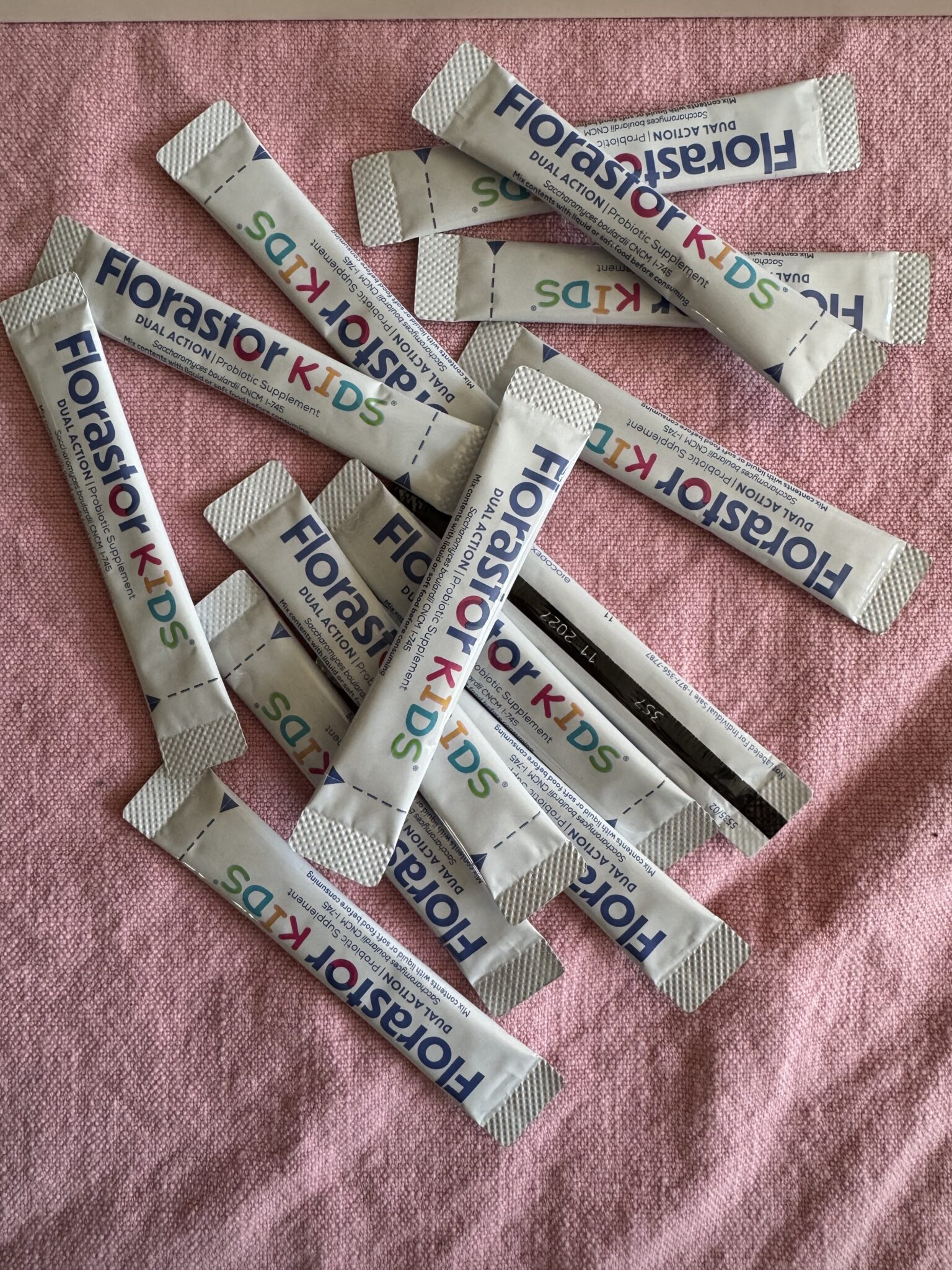 Several packets of Florastor Kids probiotic powder are scattered on a pink fabric surface.