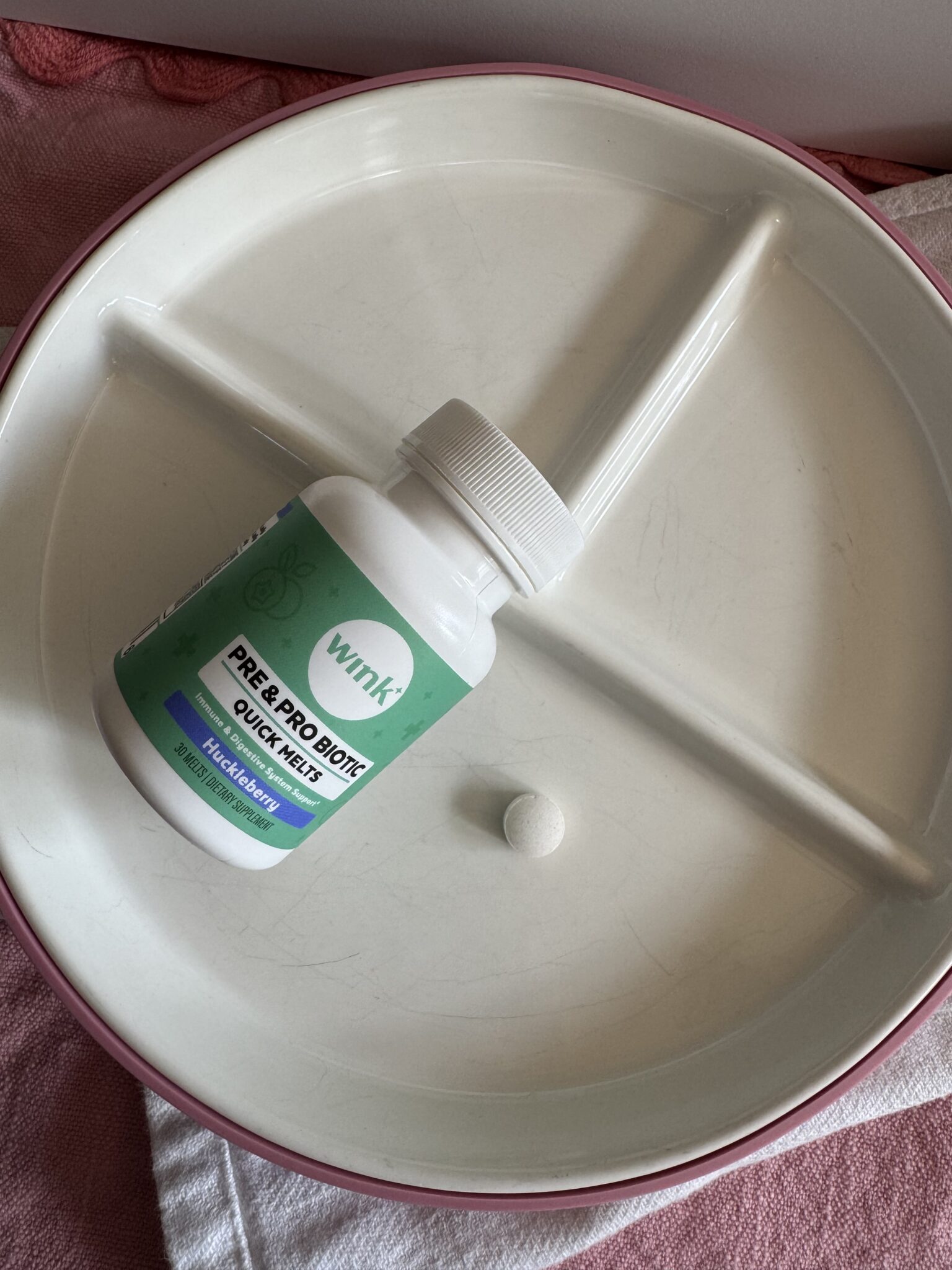 A bottle labeled "Wink! Pre & Pro Biotic Quick Melts" and a single tablet rest on a divided white plate.