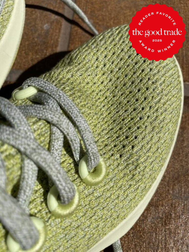 Close-up of a green knitted shoe with gray laces on a wooden floor. A red badge in the top right corner reads "Reader Favorite Award Winner 2025" from "the good trade.