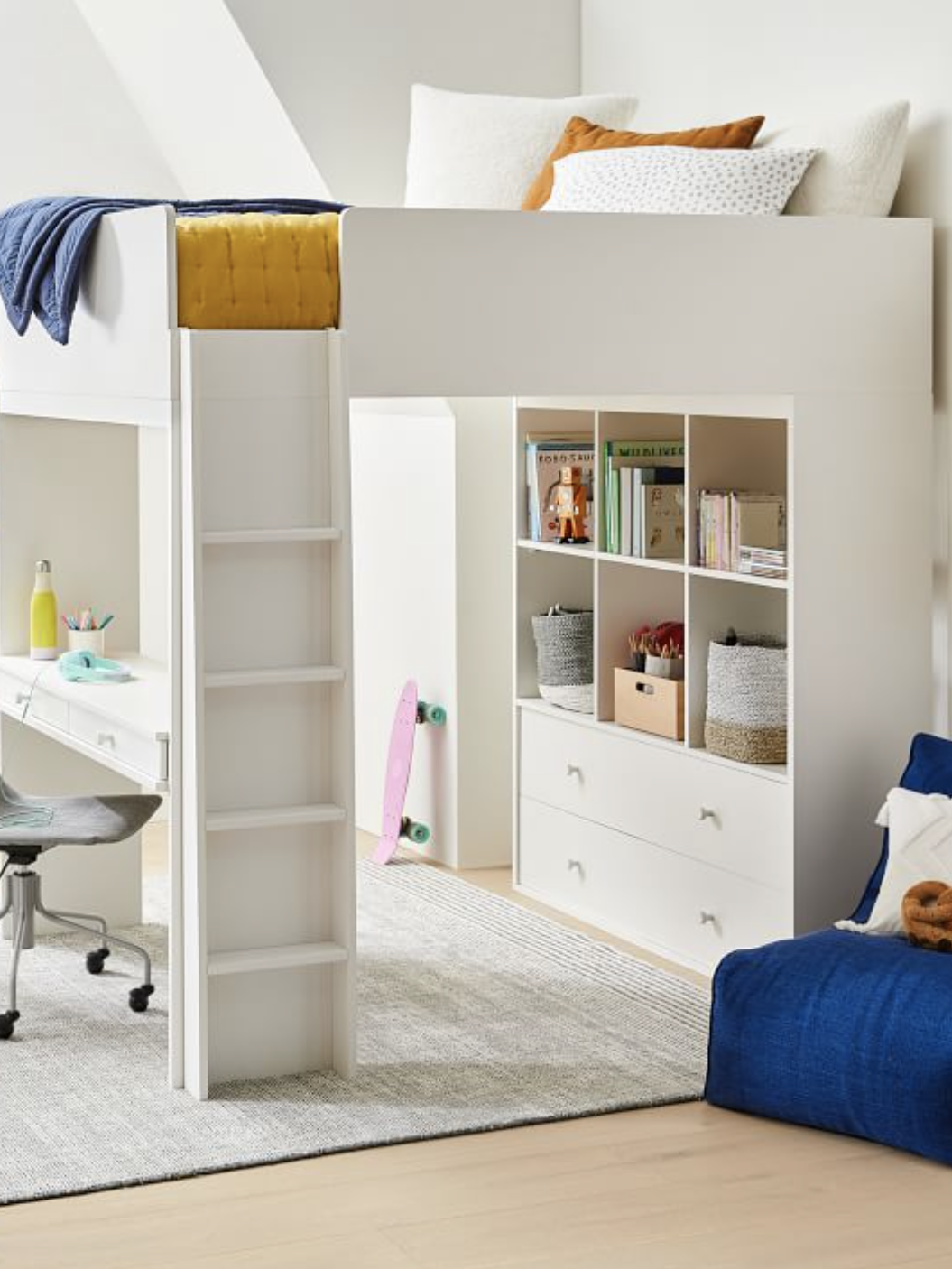 A modern loft bed with an integrated desk and shelving unit underneath, accompanied by a gray chair and blue bean bag, is set in a room with light-colored flooring and abstract wall art.