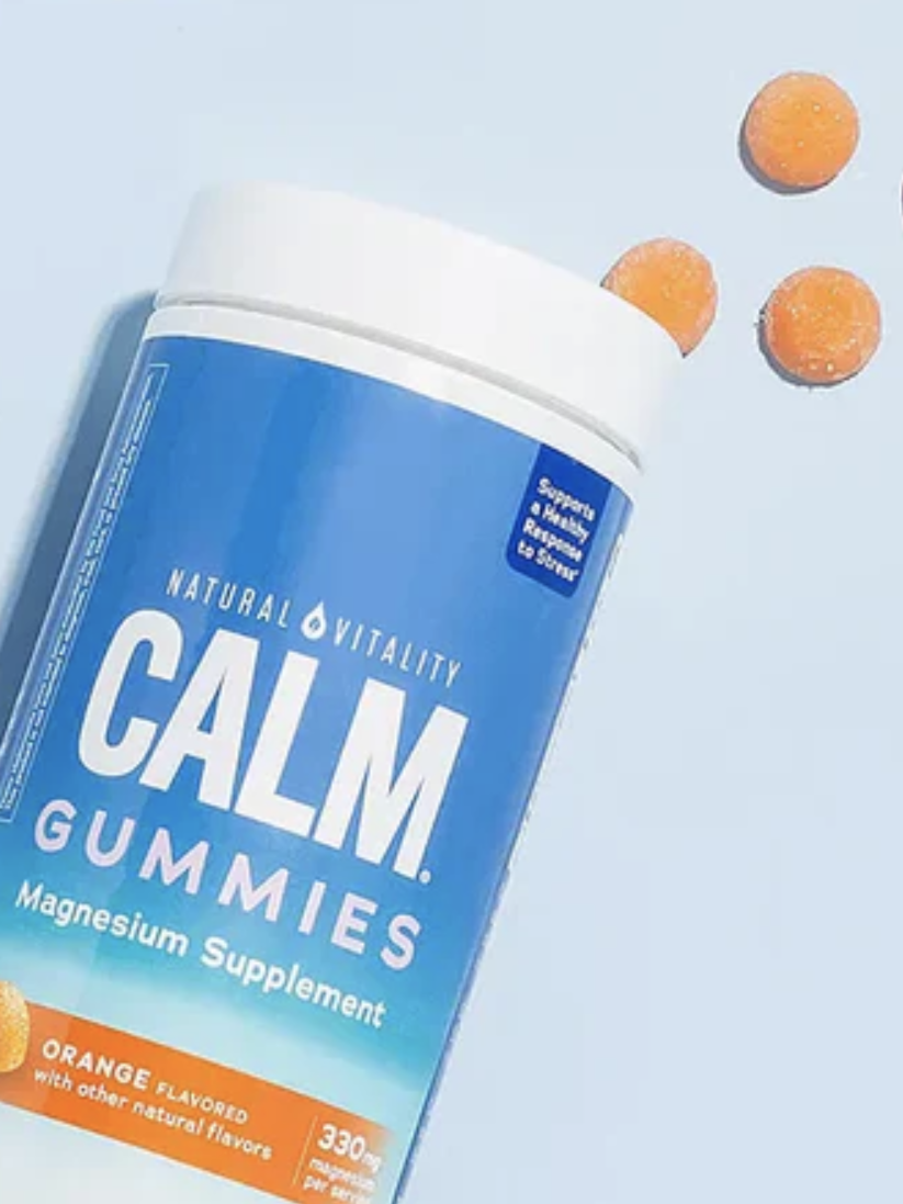 A tilted Calm Gummies container on a blue background with four orange gummies beside it. Text reads: "Enjoy Anytime. Take up to 4 gummies daily to support a healthy response to stress.