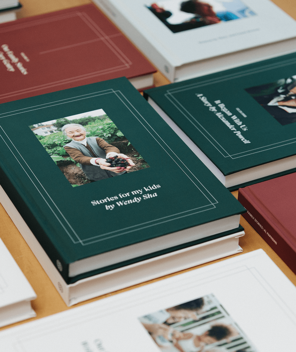 A collection of hardcover books displayed on a table, including one titled “Stories for my kids by Wendy Sha” with a cover photo of an elderly woman holding vegetables.