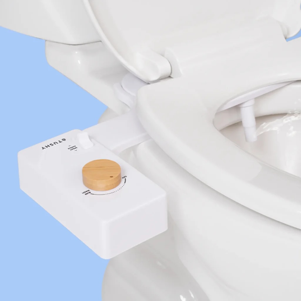 A white bidet attachment with a wooden knob is installed on a toilet, showing adjustable control and a spray nozzle inside the toilet bowl.
