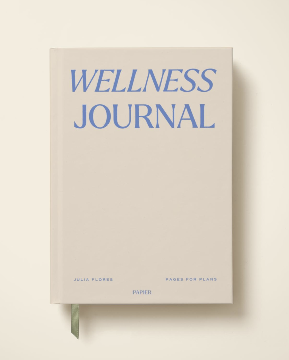 A beige book titled "Wellness Journal" with blue text and a green ribbon bookmark, authored by Julia Flores, is shown against a plain light background.