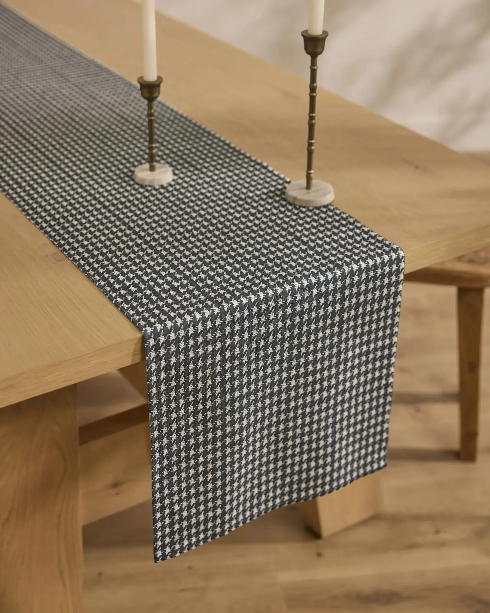 A wooden dining table with a black and white houndstooth-patterned table runner and two candlesticks placed on top.