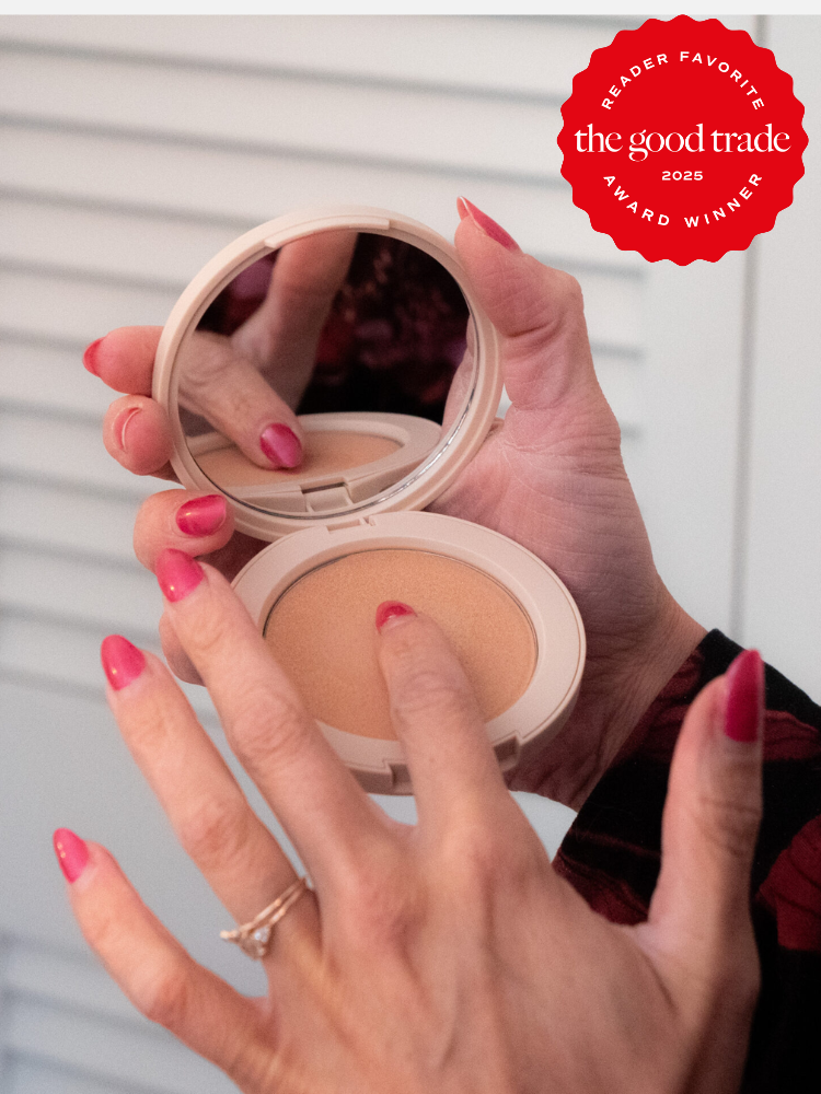 A person with red nail polish is holding and applying a compact powder using a mirror. There's a red award badge in the top right corner.