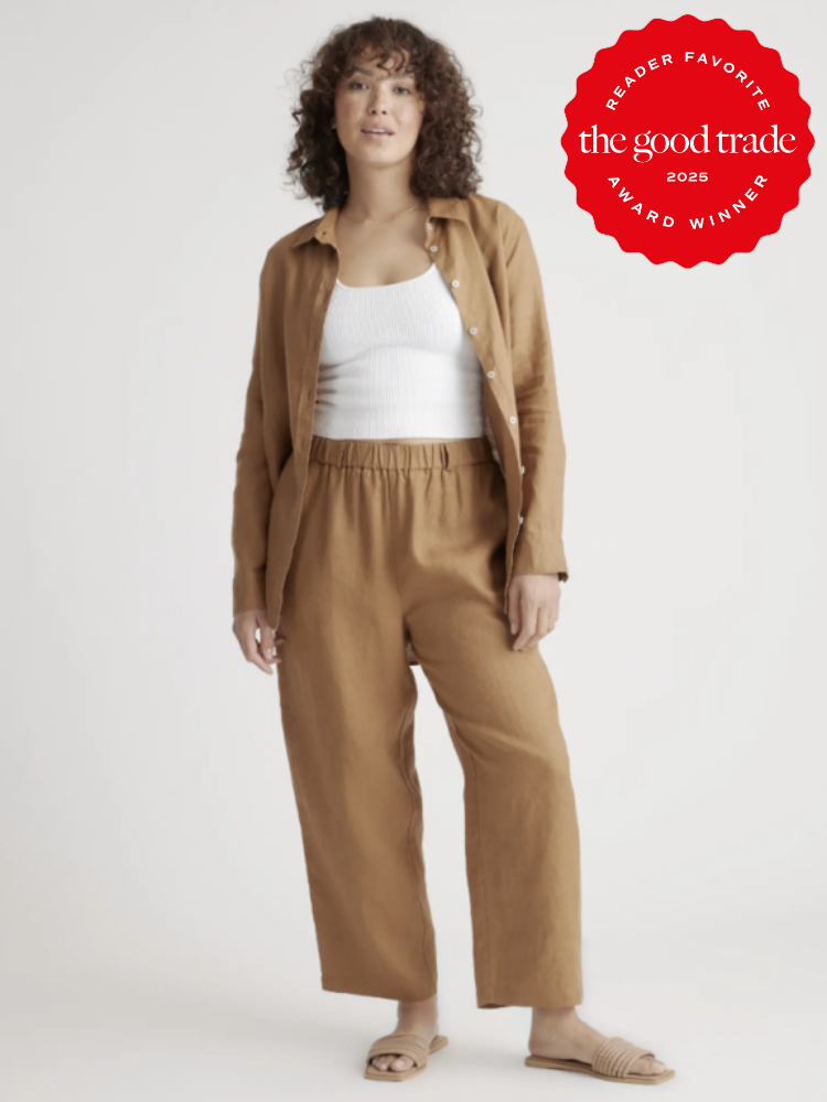 A person wearing a casual outfit stands against a plain background. They wear a brown jacket and pants with a white top. A red award badge is in the top right corner.