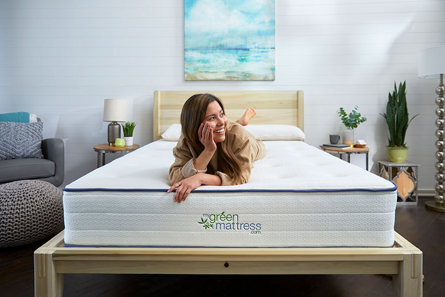 A woman lies on her stomach on a bed with a "green mattress" logo in a modern, well-lit bedroom.