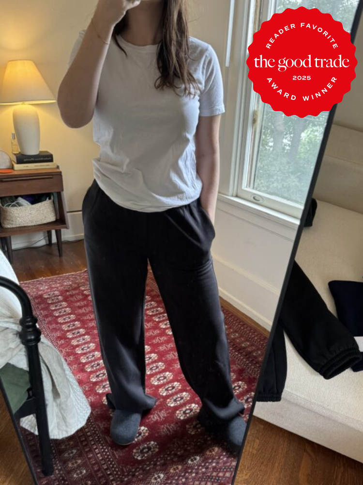 Person in white t-shirt and black pants takes mirror selfie in a room. A red award badge from "The Good Trade 2025" is placed on the image.