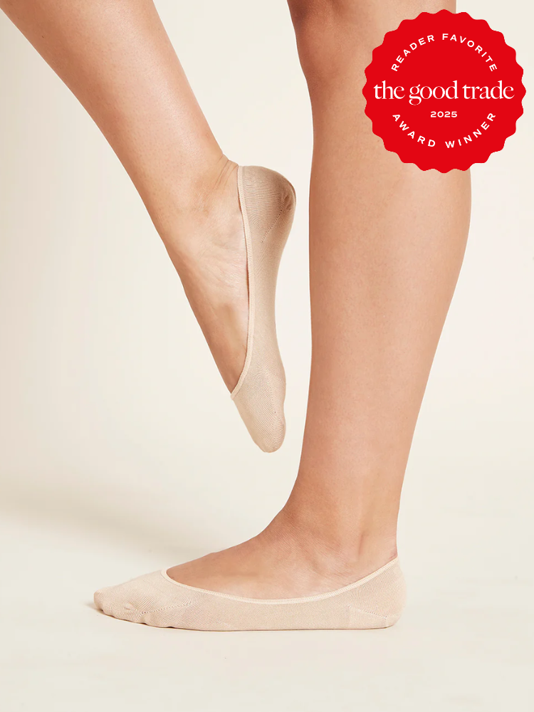 Person wearing beige organic no-show socks, with one foot raised and the other flat on the ground. "The Good Trade 2025 Award Winner" badge in the corner.