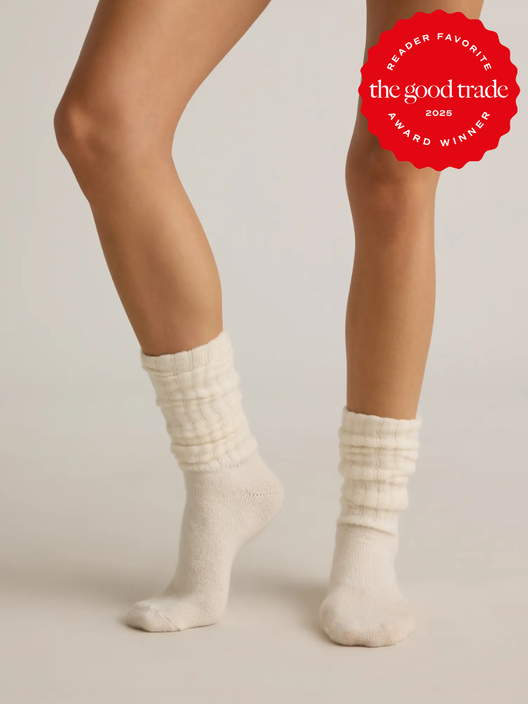 A person dons cream-colored, ribbed organic socks against a plain background. An award badge from The Good Trade graces the image, celebrating these eco-friendly socks as a 2025 reader favorite.