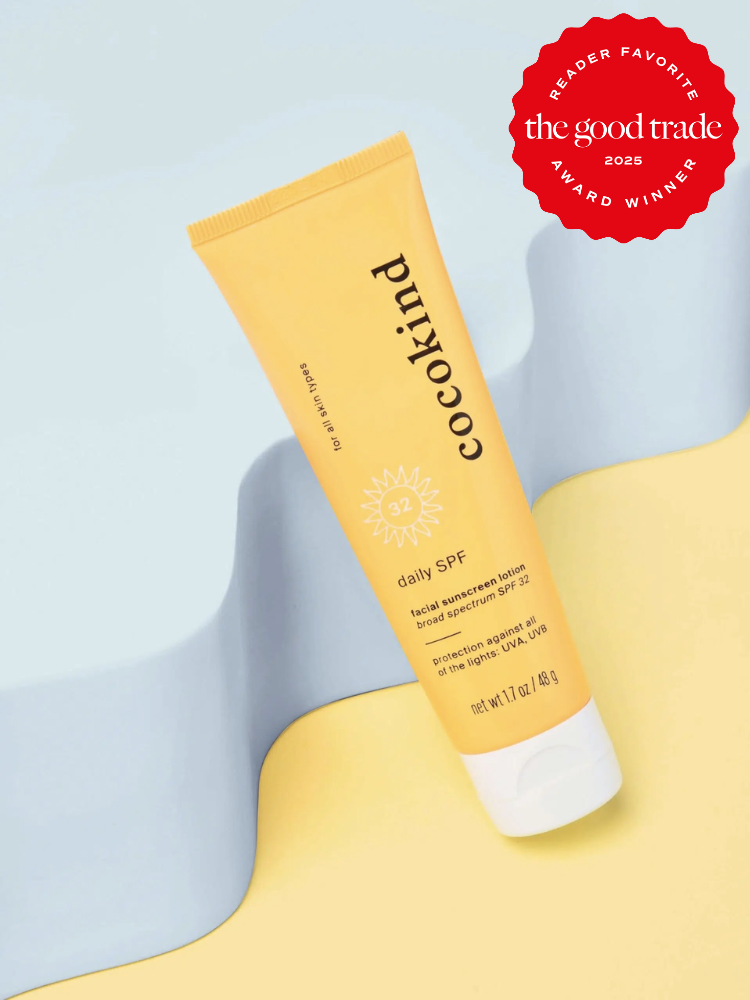 A tube of Cocokind daily SPF 32 sunscreen on a yellow and blue background. It has a "The Good Trade 2025 Award Winner" badge.