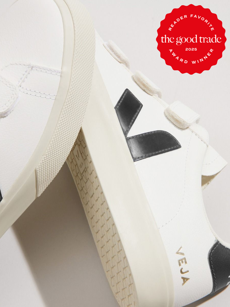 Close-up of white Veja sneakers with black logo on the side. The good trade award winner badge is visible in the top right corner.